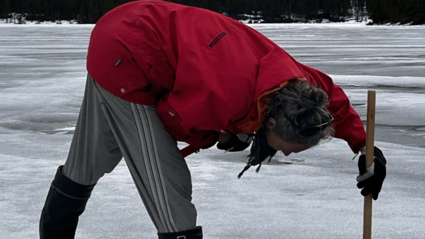 a person measuring ice thickness with a stick