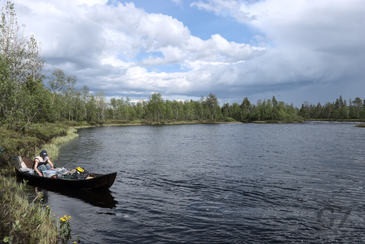 Loading boat at river shore Person in loaded wooden rowing boat, next to a river shore